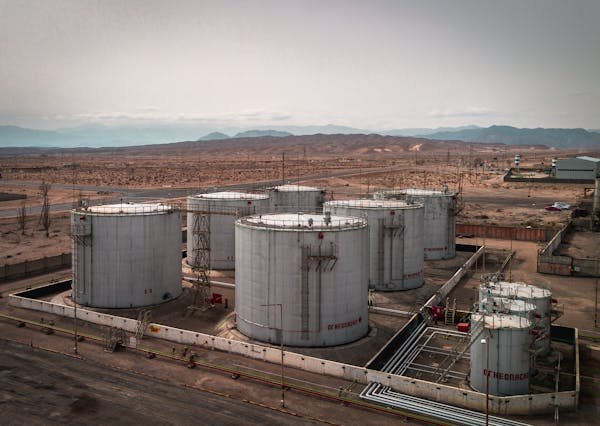 Aerial view of large industrial oil tanks in a desert setting with mountains in the distance.