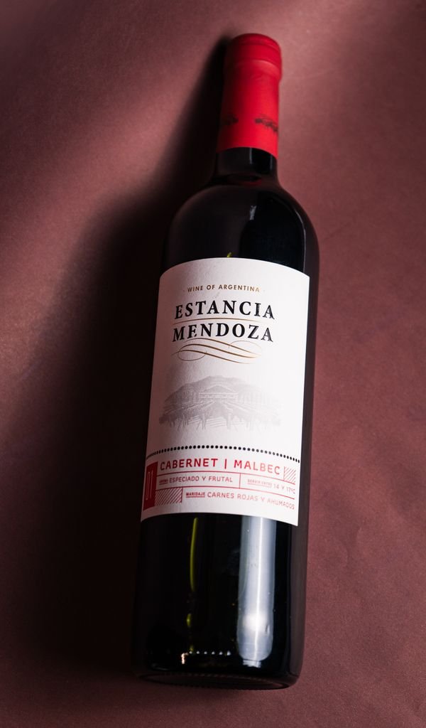 A vertical shot of an Estancia Mendoza wine bottle featuring a Cabernet Malbec blend on a red background in Mendoza, Argentina.